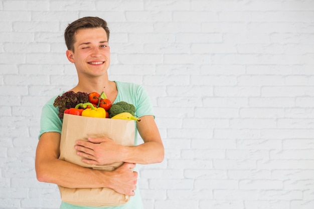 Man holding grocery bag full of fruits and vegetable winking