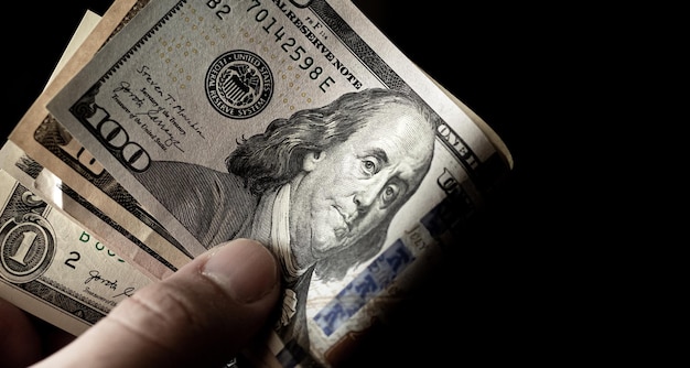 A man holding in hand a group of Us dollar banknotes with black background