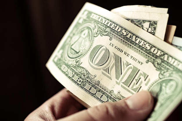 A man holding in hand a group of Us dollar banknotes with black background