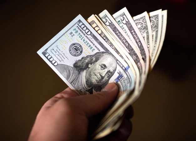 A man holding in hand a group of Us dollar banknotes with dark background