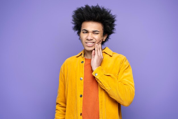 Man holding hand on his cheek having a toothache  isolated on purple background. Dental care