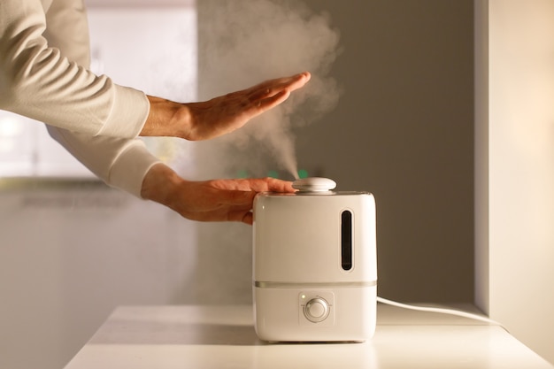 Man holding hand over steam aroma oil diffuser on the table at home, steam from the air humidifier