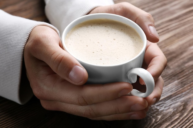 木製の背景にコーヒーのカップを手に持っている男