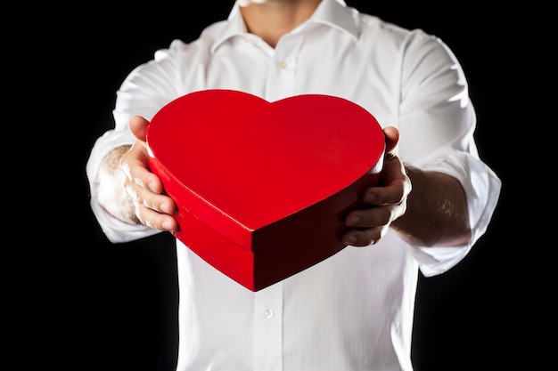 Мужчина держит подарочную коробку сердца в жесте дарения.