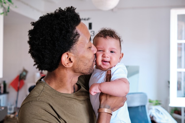 Man holding his baby in his arms while giving him a kiss.