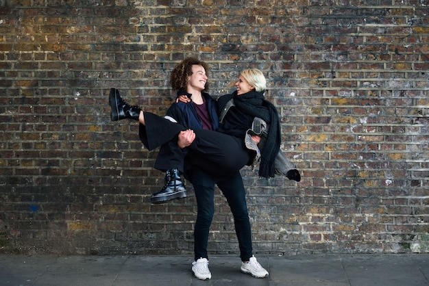 Man holding his girlfriend in his arms in front of a brick wall typical of London