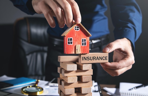 Photo man holding house model with a text insurance on wooden block.