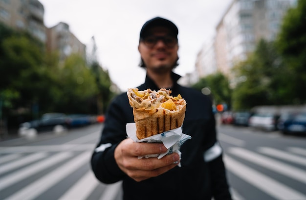 Foto uomo con un panino di kebab in mano per strada