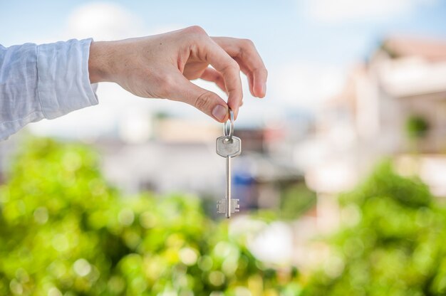 Мужчина держит ключ к дому на фоне домов в городе. сделка с концепцией недвижимости