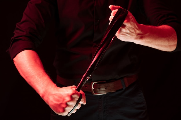 A man holding a leather whip. bdsm