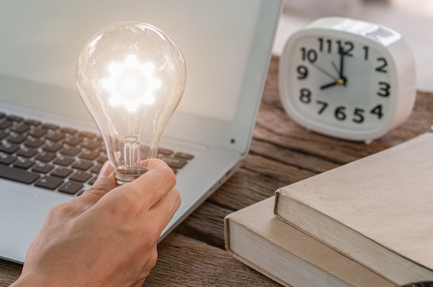 Foto un uomo che tiene un simbolo dell'ingranaggio della lampadina durante l'utilizzo di un computer