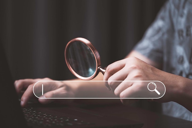 Photo man holding magnifier glass and using computer laptop with search bar icon for search engine optimization or seo concept to find information by internet connection