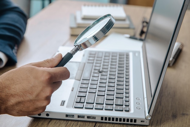 Man holding magnifier with laptop