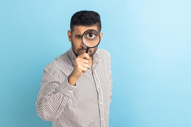 Man holding magnifying glass and looking at camera with big zoom eye having strict bossy expression