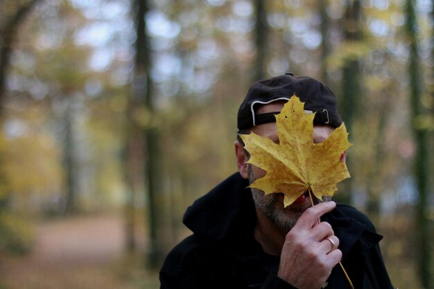 Фото Мужчина, держащий кленовый лист над лицом осенью