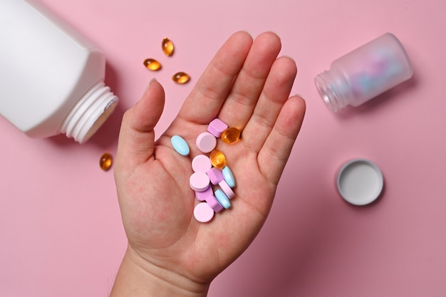Man holding medical pills and vitamins on pink background.