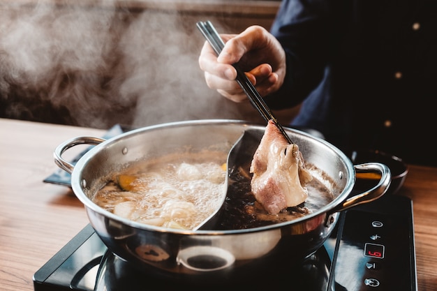 鍋でしゃぶしゃぶ鍋から中珍スライス和牛A5牛肉を握って男。