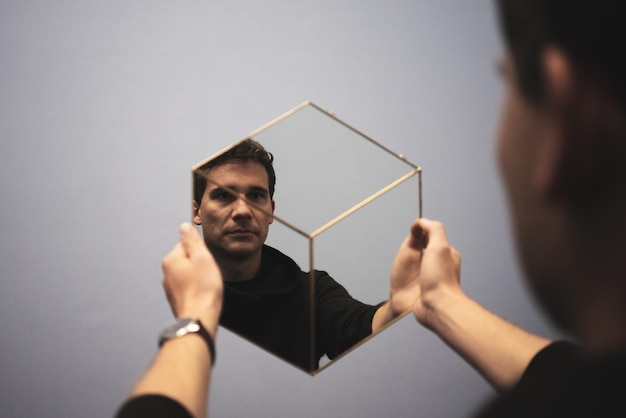 man holding mirror with reflection against white wall