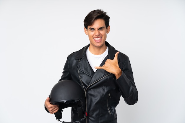 Man holding a motorcycle helmet over isolated white wall making phone gesture