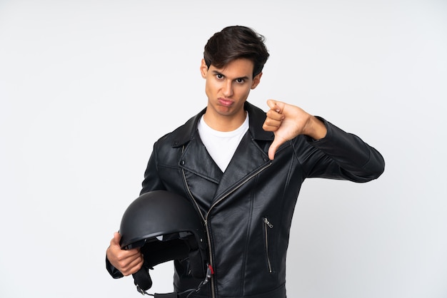 Man holding a motorcycle helmet over white wall showing thumb down sign