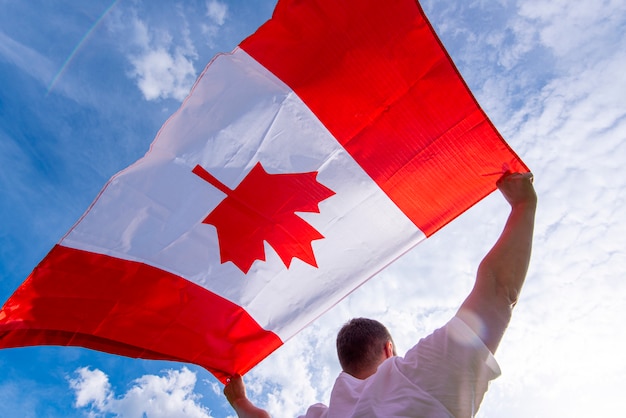 Photo man holding the national flag of canada against blue sky