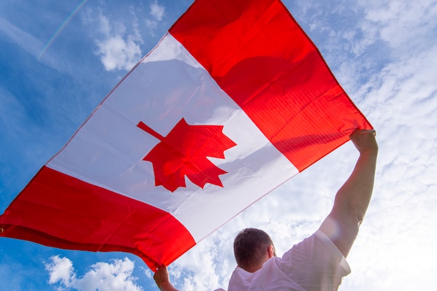 Man holding The National Flag of Canada against blue sky