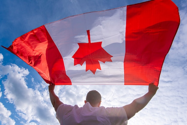 Photo man holding the national flag of canada against blue sky