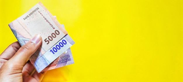 Man holding new Indonesian banknotes Rp5000 and Rp10000 rupiah isolated on a yellow background