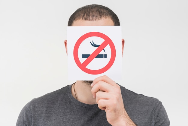 Photo a man holding no smoking sign in front of his face against white backdrop