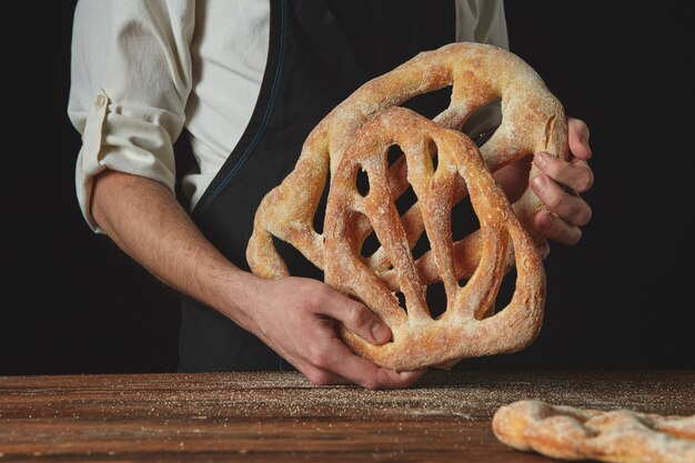 Uomo che tiene organico delizioso pane fougas su uno sfondo scuro