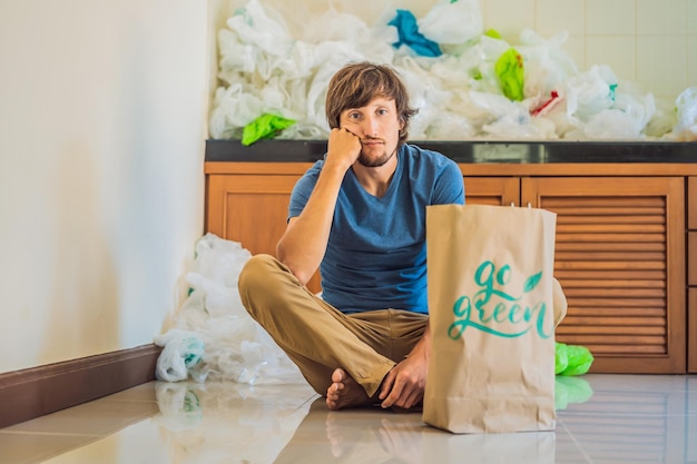 Uomo che tiene un pacco con la scritta go green in mezzo a una pila di sacchetti di plastica concetto di zero rifiuti il concetto di giornata mondiale dell'ambiente