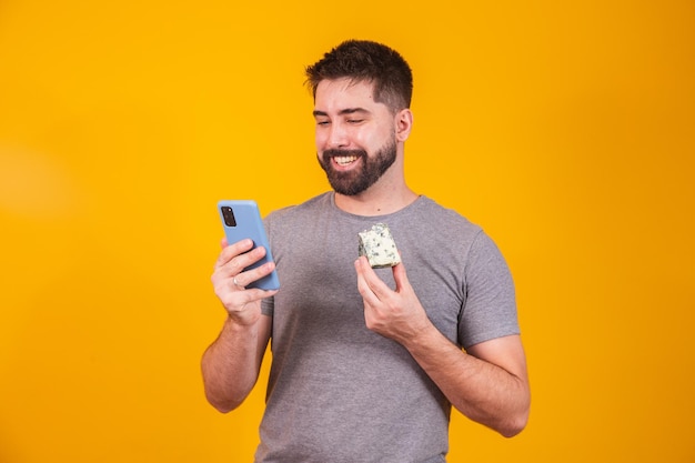 Man holding a piece of cheese in one hand and using her cell phone with the other