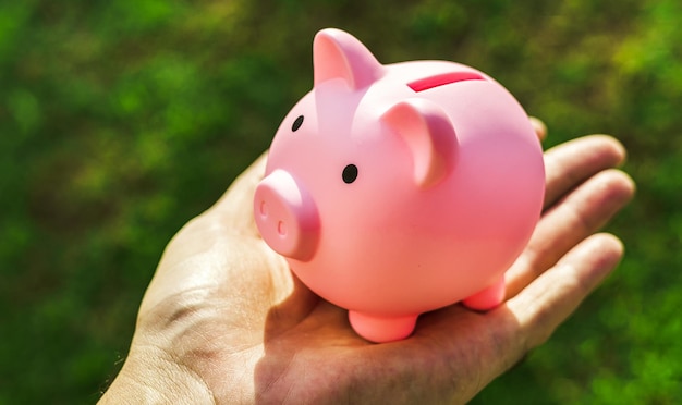 A man holding a piggy bank in his hand and a green grass in the background