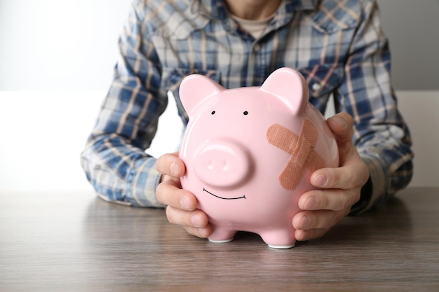 man holding piggy bank with adhesive bandage on white background