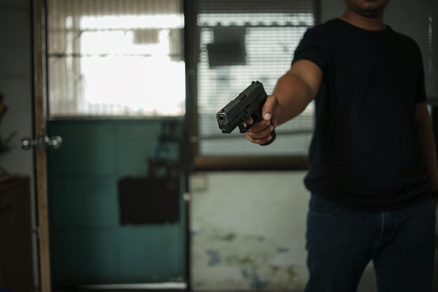 Man holding a pistol standing in a room in blackconcept of assassination murder criminal