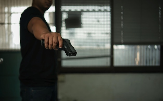 Photo man holding a pistol standing in a room in blackconcept of assassination murder criminal