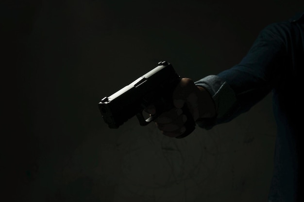 Человек с пистолетом, стоящий в комнате в черном, концепция убийства преступника