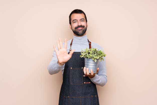 Man holding a plant over isolated background counting five with fingers