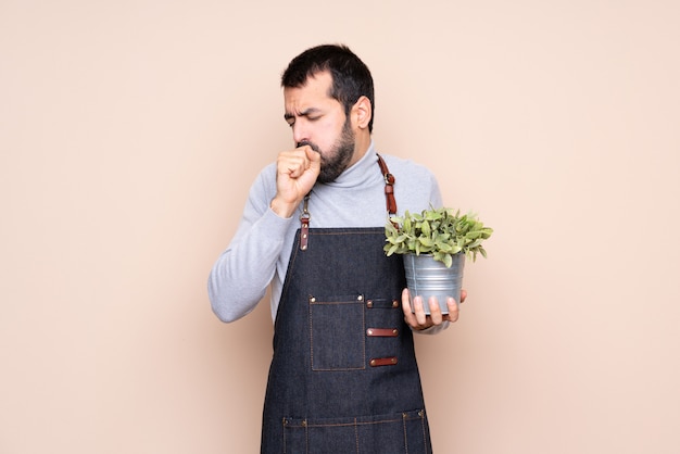 Man holding a plant over isolated wall is suffering with cough and feeling bad