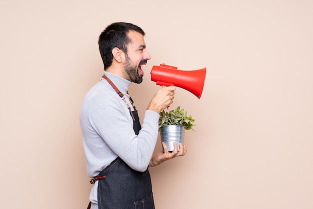 Man holding a plant over isolated wall shouting through a megaphone