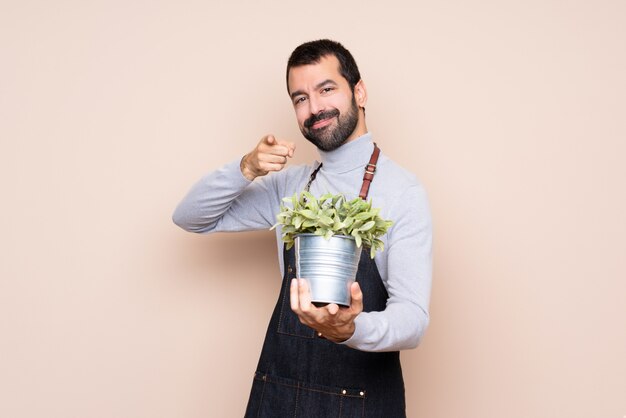 Man holding a plant points finger at you while smiling