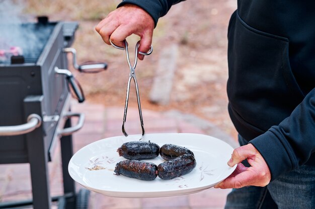 Man holding a plate with some blood sausages cooked on the barbecue.