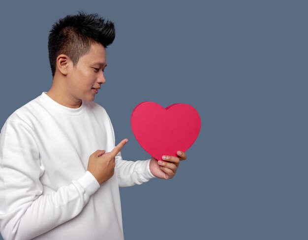 Man holding and pointing red heart shape isolated on plain background