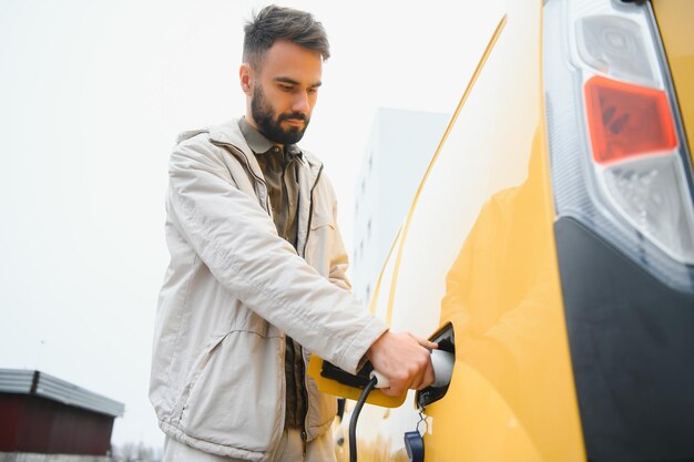 Man Holding Power Charging Cable For Electric Car In Outdoor Car Park And he s going to connect the car to the charging station in the parking lot near the shopping center