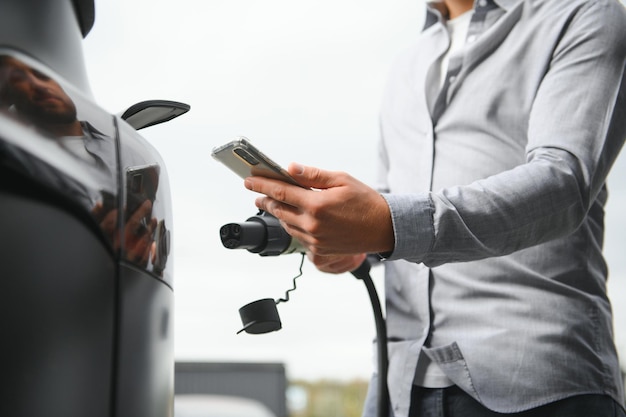 Photo man holding power charging cable for electric car in outdoor car park