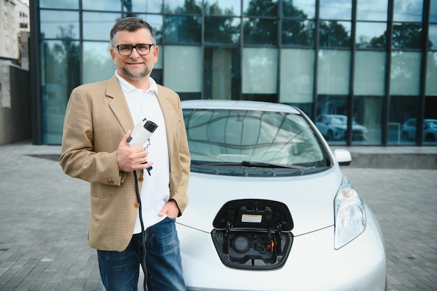 Uomo che tiene il connettore di alimentazione per auto elettrica