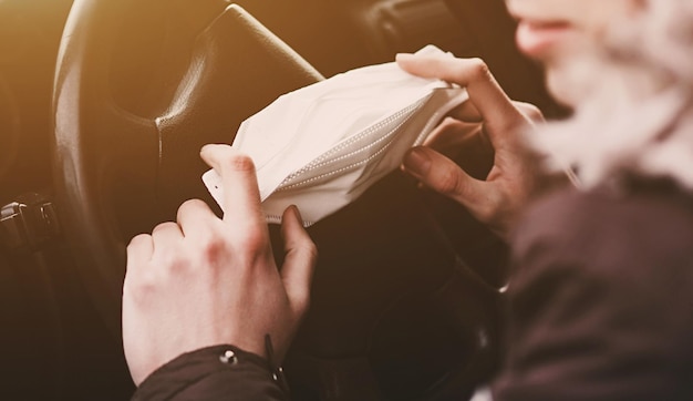 Man holding protective mask in hand to avoid the infection of virus and polluted air spreading deseases inside of his car. Health care, coronavirus.