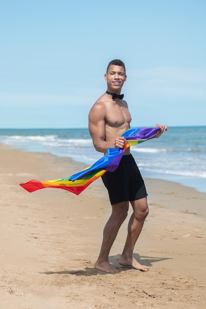 Man holding a rainbow gay pride flag while standing on the beach