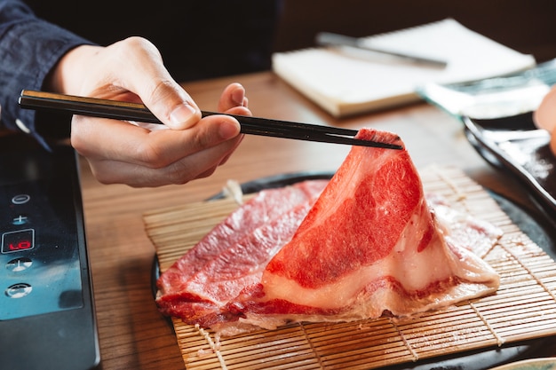 Man holding rare slice Wagyu A5 beef by chopsticks for boiling in Shabu hot pot.  