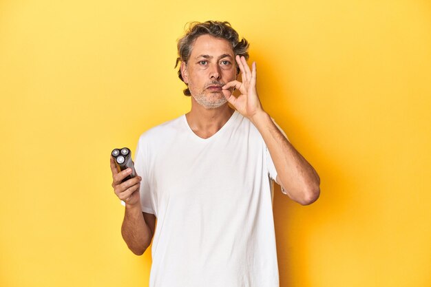 Man holding a razor yellow studio background with fingers on lips keeping a secret